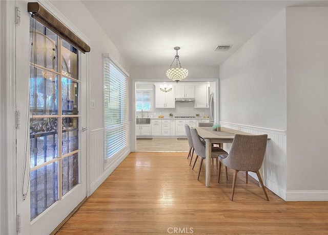 dining area featuring light wood-style floors, wainscoting, and visible vents