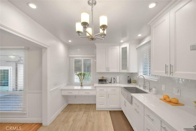 kitchen with decorative light fixtures, light countertops, glass insert cabinets, white cabinetry, and a sink