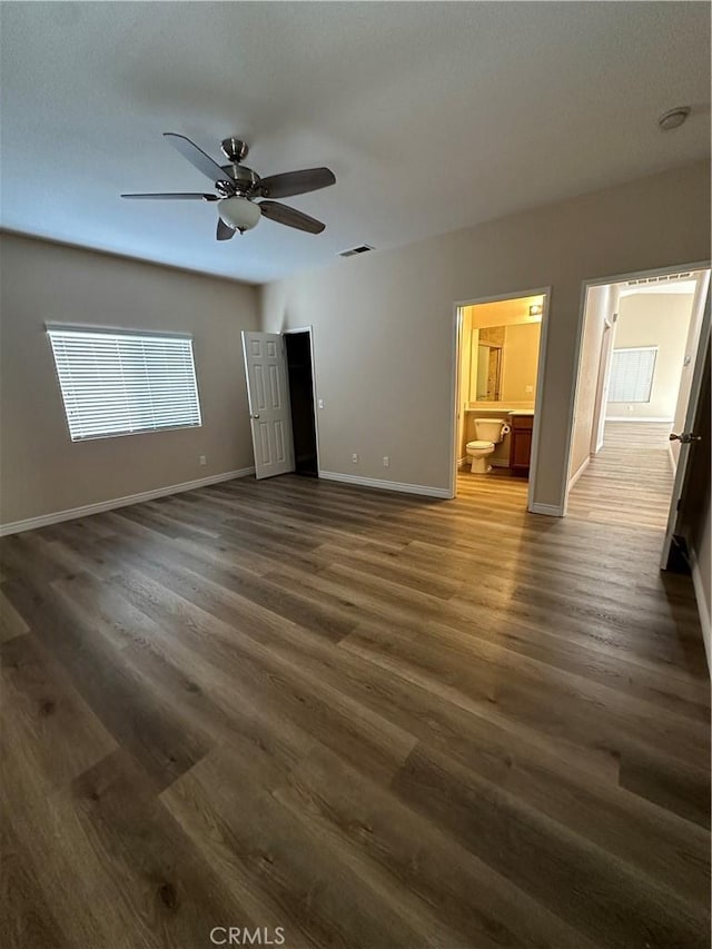 unfurnished bedroom with ensuite bath, ceiling fan, and dark wood-type flooring