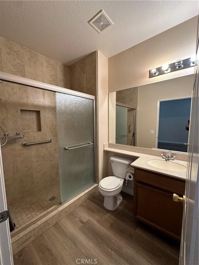 bathroom featuring toilet, wood-type flooring, a textured ceiling, and a shower with shower door