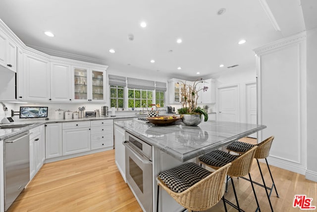 kitchen featuring white cabinetry, appliances with stainless steel finishes, light wood-type flooring, a kitchen island, and light stone counters