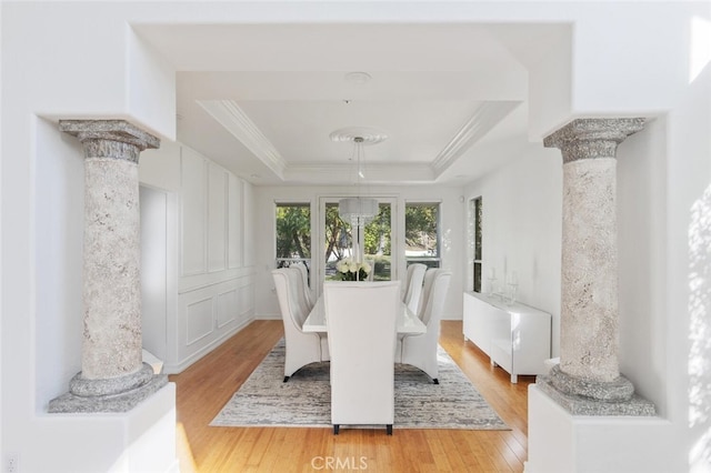 dining room with ornamental molding, wood-type flooring, a tray ceiling, and decorative columns