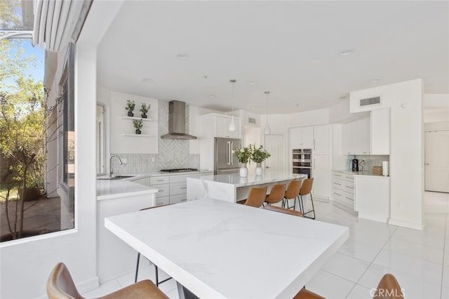 kitchen with wall chimney range hood, appliances with stainless steel finishes, white cabinetry, a kitchen breakfast bar, and a kitchen island