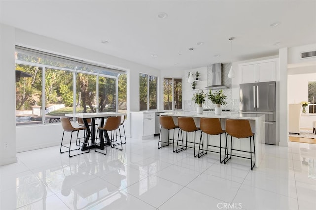 kitchen with stainless steel appliances, a kitchen island, white cabinets, and wall chimney exhaust hood