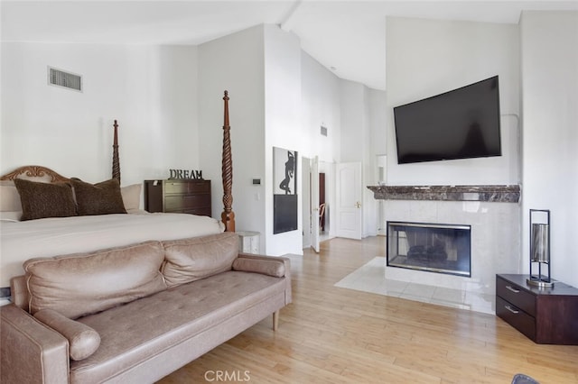 bedroom with beam ceiling, a fireplace, high vaulted ceiling, and light wood-type flooring