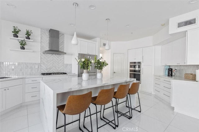 kitchen featuring decorative light fixtures, appliances with stainless steel finishes, a kitchen island, wall chimney range hood, and white cabinets