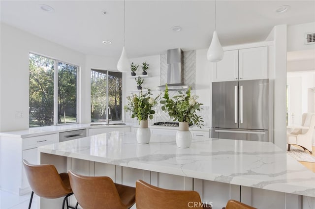 kitchen with pendant lighting, wall chimney range hood, sink, stainless steel appliances, and white cabinets