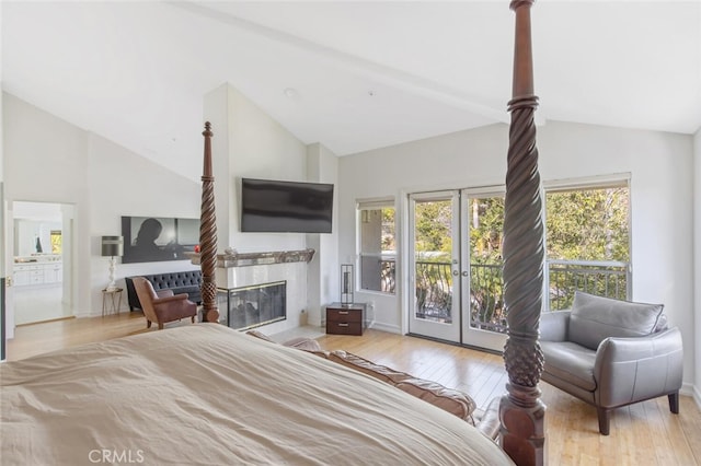 bedroom with high vaulted ceiling, access to outside, a premium fireplace, light wood-type flooring, and french doors