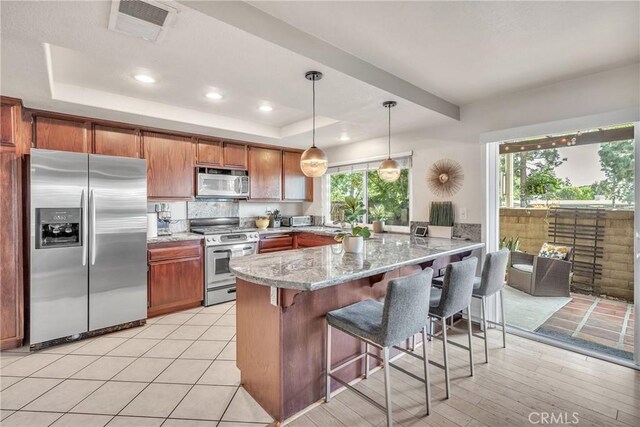 kitchen featuring decorative light fixtures, kitchen peninsula, a tray ceiling, stainless steel appliances, and light stone counters