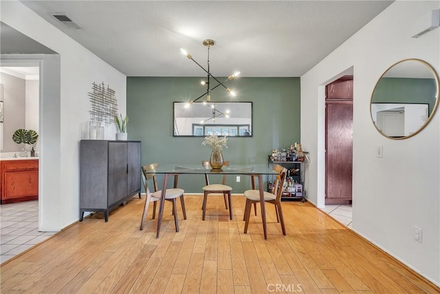 dining area with crown molding, an inviting chandelier, and light hardwood / wood-style floors