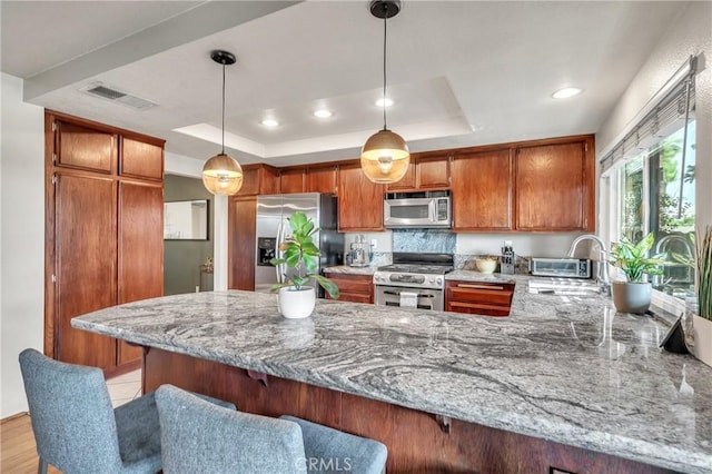 kitchen with hanging light fixtures, kitchen peninsula, appliances with stainless steel finishes, and a tray ceiling