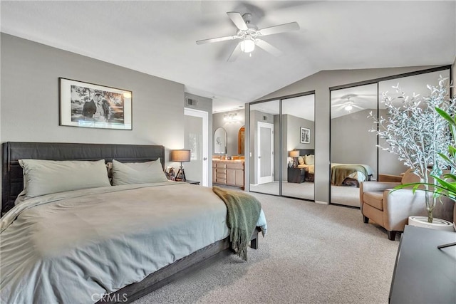 carpeted bedroom featuring vaulted ceiling, ceiling fan, ensuite bathroom, and two closets