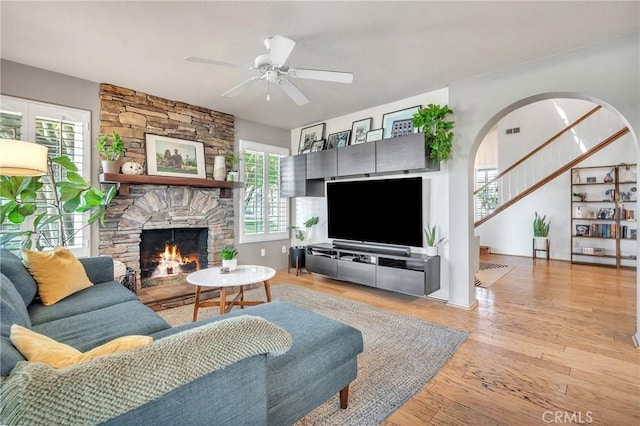 living room with ceiling fan, a stone fireplace, and light wood-type flooring