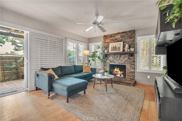 living room with ceiling fan, light wood-type flooring, and a stone fireplace