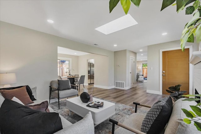 living room featuring a wealth of natural light, a skylight, and light hardwood / wood-style flooring