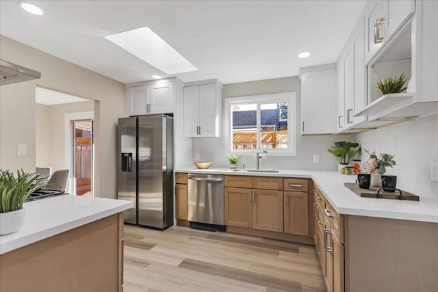 kitchen featuring white cabinets, a skylight, stainless steel appliances, sink, and light wood-type flooring