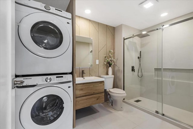 bathroom featuring toilet, vanity, tile patterned flooring, a shower with shower door, and stacked washing maching and dryer