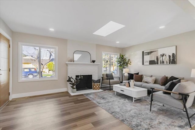 living room with a brick fireplace, a skylight, and hardwood / wood-style floors