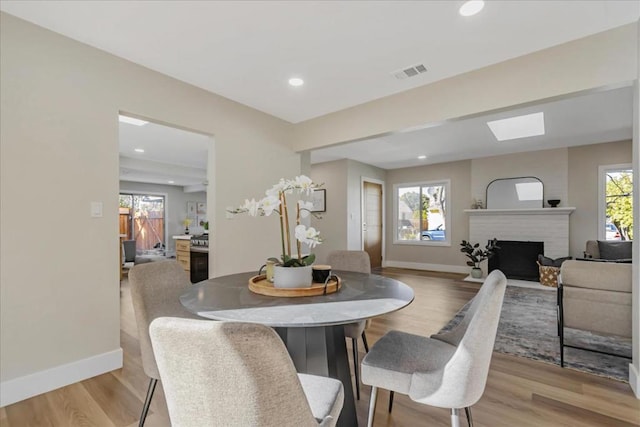 dining room featuring a skylight, a fireplace, and light hardwood / wood-style flooring