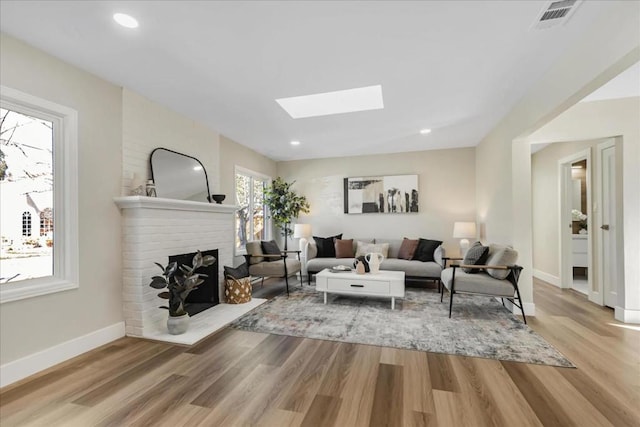 living room with a skylight, a fireplace, and light hardwood / wood-style flooring