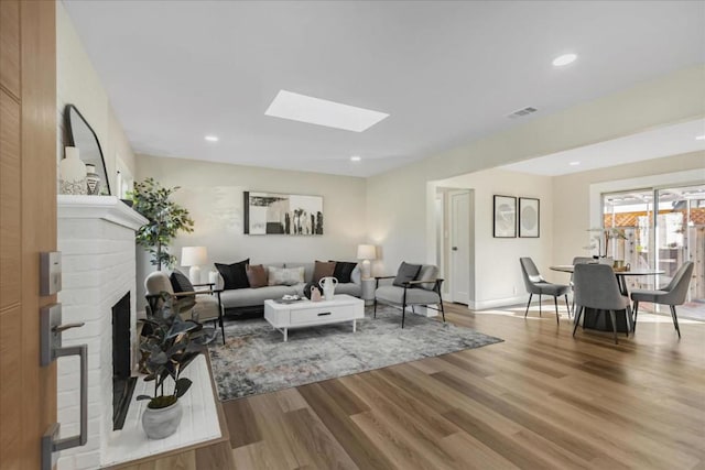 living room featuring a skylight, a brick fireplace, and hardwood / wood-style floors