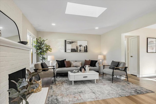 living room featuring a brick fireplace, wood-type flooring, and a skylight