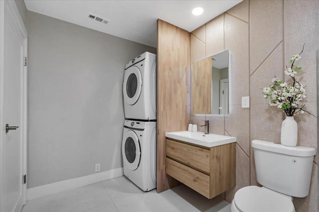 bathroom with stacked washing maching and dryer, toilet, tile patterned floors, and vanity