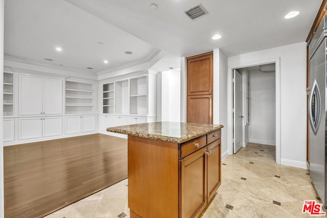 kitchen with stainless steel refrigerator, light stone countertops, a center island, light tile patterned flooring, and ornamental molding