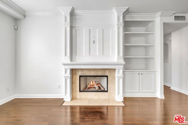 unfurnished living room with built in shelves, a premium fireplace, hardwood / wood-style floors, and ornamental molding