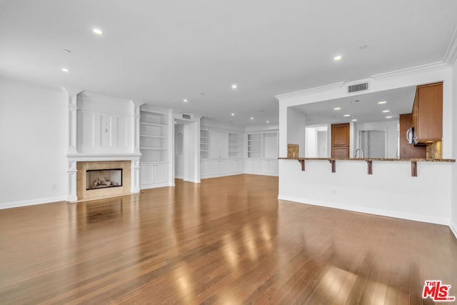 unfurnished living room with light wood-type flooring, built in features, ornamental molding, and a premium fireplace