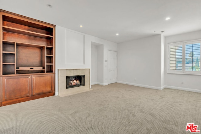 unfurnished living room featuring light carpet, built in shelves, and a tiled fireplace