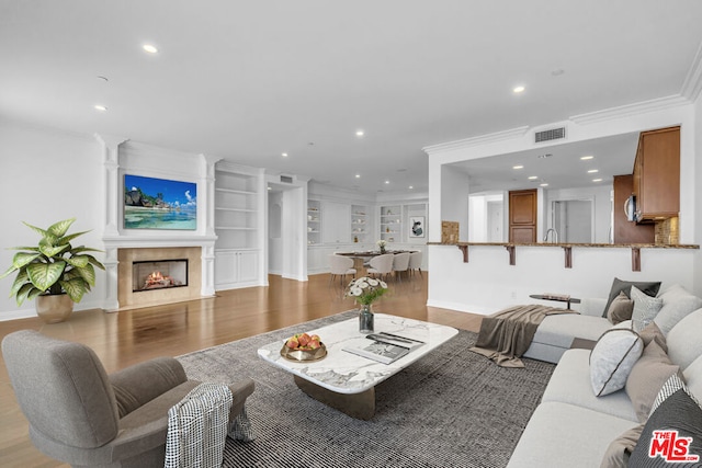 living room with built in shelves, crown molding, light hardwood / wood-style flooring, and a premium fireplace