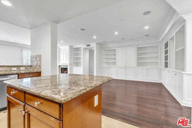 kitchen with light stone countertops, ornamental molding, a kitchen island, and stainless steel dishwasher