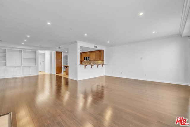 unfurnished living room featuring built in shelves, light hardwood / wood-style floors, and ornamental molding