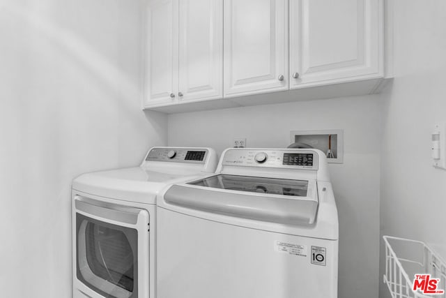 clothes washing area with washer and clothes dryer and cabinets