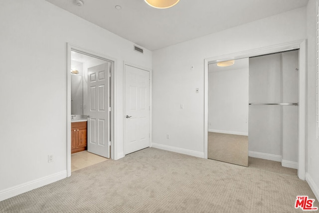 unfurnished bedroom with ensuite bath, a closet, and light colored carpet