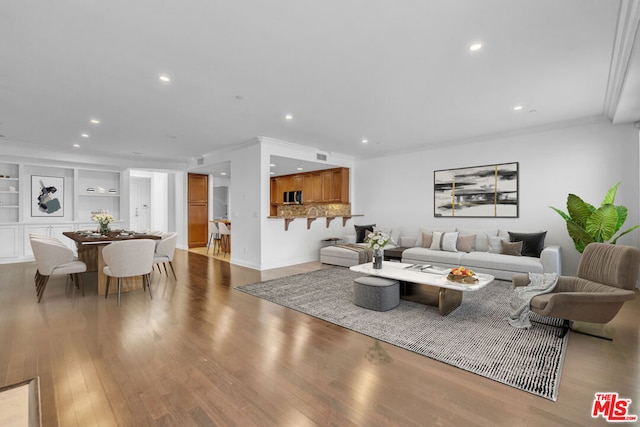 living room featuring built in shelves, ornamental molding, and hardwood / wood-style floors