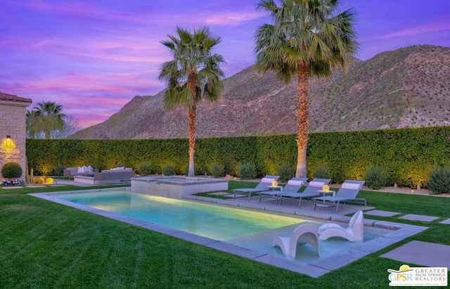 pool at dusk featuring a mountain view, an in ground hot tub, and a lawn