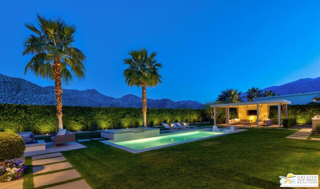 view of swimming pool with a mountain view, a patio area, an outdoor living space with a fireplace, a yard, and an in ground hot tub