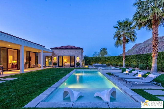 pool at dusk featuring a patio area, a mountain view, and a lawn