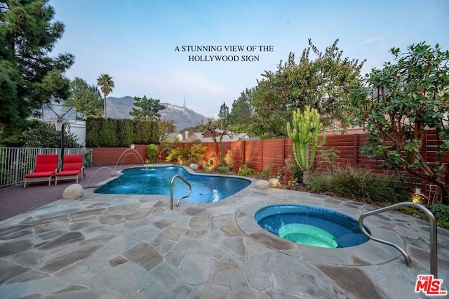 view of pool featuring pool water feature, a mountain view, a patio, and an in ground hot tub