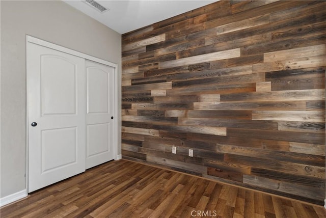 unfurnished bedroom featuring a closet, dark hardwood / wood-style floors, and wooden walls