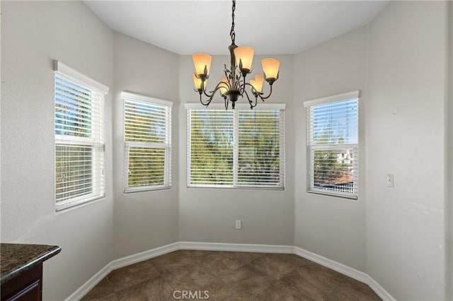 unfurnished dining area featuring plenty of natural light, dark tile patterned flooring, and a notable chandelier