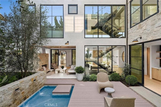 rear view of property with an outdoor pool, a wooden deck, and stucco siding