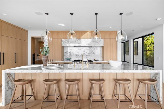 kitchen featuring light stone counters, backsplash, pendant lighting, and a spacious island