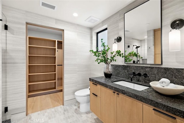 bathroom with toilet, vanity, tile walls, and tile patterned floors