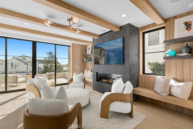 living room with a large fireplace, wood walls, beamed ceiling, and light wood-type flooring