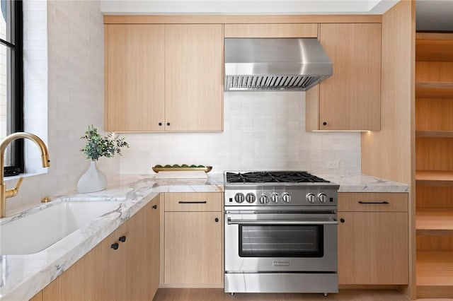 kitchen featuring stainless steel range, wall chimney exhaust hood, light brown cabinets, and sink