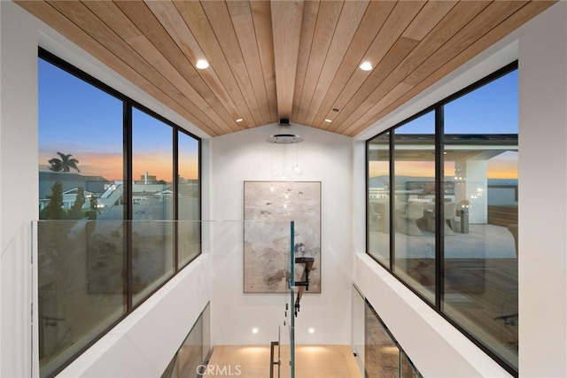 hallway featuring lofted ceiling, a healthy amount of sunlight, and wooden ceiling