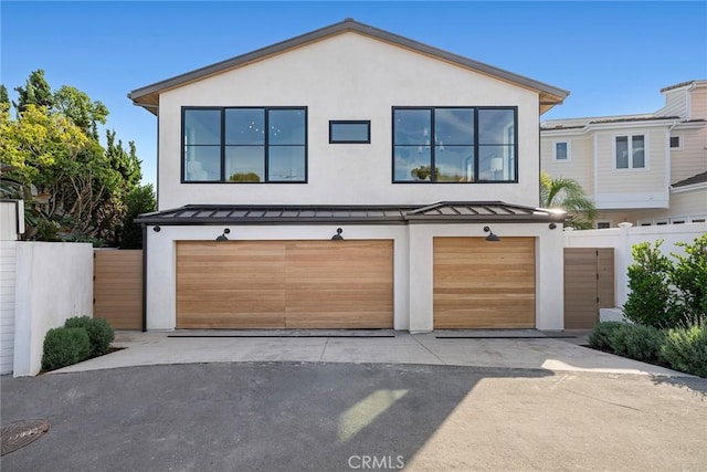 view of front of property with a garage, aphalt driveway, a standing seam roof, metal roof, and fence
